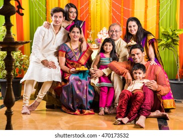 Happy Indian Family Celebrating Ganesh Festival or Chaturthi - Welcoming or performing Pooja and eating sweets in traditional wear at home decorated with Marigold Flowers