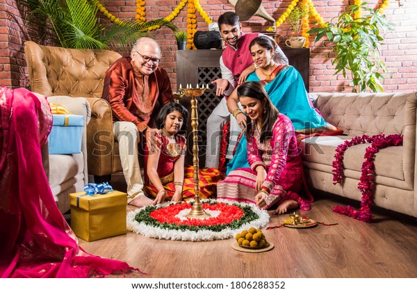Happy Indian Family\
Celebrating Ganesh Festival or Chaturthi - Welcoming or performing\
Pooja and eating sweets in traditional wear at home decorated with\
Marigold Flowers