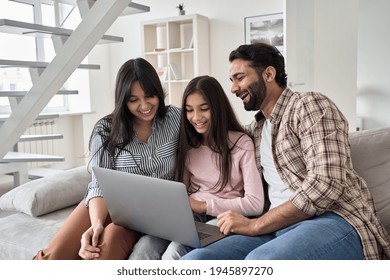 Happy Indian Family With Child Daughter Having Fun Using Laptop Computer At Home. Smiling Parents And Teen Kid Daughter Laughing Looking At Device Browsing Or Watching Funny Videos Sitting On Sofa.