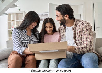 Happy Indian Family With Child Daughter Unpacking Parcel At Home. Smiling Parents And Teen Kid Daughter Opening Postal Box Looking At Gift In Online Shopping Delivery Package Sitting On Sofa Together.