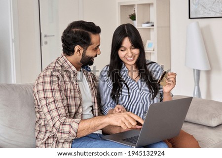 Happy indian family couple shoppers customers using laptop computer doing ecommerce shopping together at home. Smiling husband and wife consumers holding credit card buying online, making e payments.