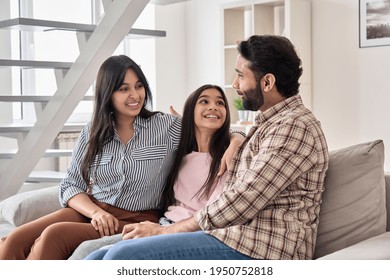 Happy Indian Family Couple With Teen Child Daughter Bonding, Hugging, Talking Sitting On Couch At Home. Smiling Husband And Wife Embracing Child Spending Time Together Relaxing On Sofa In Living Room