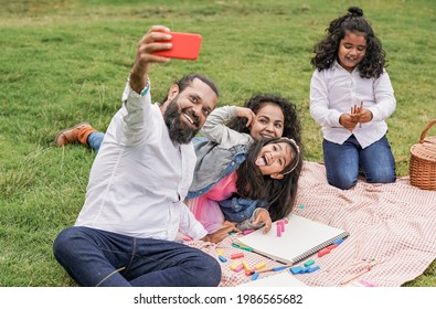 Happy Indian Family Enjoy Day Outdoor At City Park With Pic Nic And Toys While Taking A Selfie With Smartphone - Family, Parents And Children Love