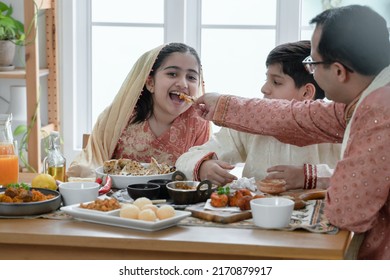 Happy Indian Family Enjoy Eating Food With Hands, Selective Focus On Asian Cute Girl Eating Naan Bread Dipping In Curry From Father Feeding, Wear Traditional Clothes, Sitting With Brother At Home