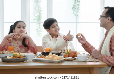 Happy Indian Family Enjoy Eating Food With Hands, South Asian Father And Children Wear Traditional Clothes, Sitting At Dining Table At Home Together. Indian Culture Lifestyle.