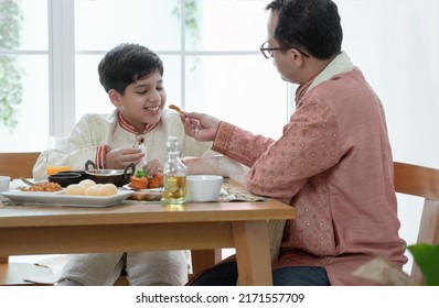 Happy Indian Family Enjoy Eating Food With Hands, Selective Focus On South Asian Cute Boy Eating Naan Bread Dipping In Curry From Father Feeding, Wear Traditional Clothes, Sitting At Dining Table