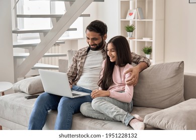 Happy Indian Family Father With Teenage Child Daughter Having Fun Using Laptop Computer At Home Watching Tv Movie, Browsing Internet, E Learning, Having Video Zoom Call Sit On Sofa In Living Room