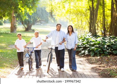 Happy Indian Family Of Four Walking Outdoors In The Park