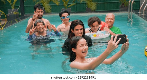 Happy Indian family having fun and enjoying outdoor picnic. Teen girl taking selfie with senior parents using mobile smartphone at water park. Cute Child relax in colorful toy floating ring at resort. - Powered by Shutterstock