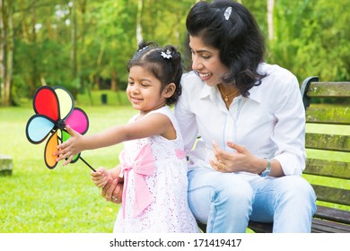 Happy Indian Family Outdoor Activity. Candid Portrait Of Mother And Daughter Playing Windmill At Garden Park.