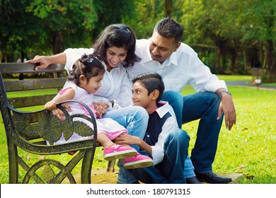 Happy Indian Family At Outdoor Park. Candid Portrait Of Parents And Children Having Fun At Garden Park.