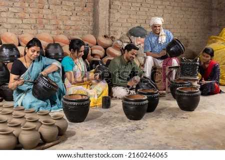 Happy Indian family of potters painting and polishing pot together at workshop