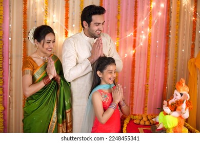 A happy Indian family seeking blessings from Lord Ganesha on Ganesh Chaturthi - Praying with folded hands. Stunning and beautiful family in Indian ethnic dress worshiping Lord Ganesha on Ganesh Cha...