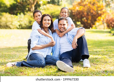 Happy Indian Family Sitting On Grass In The Park