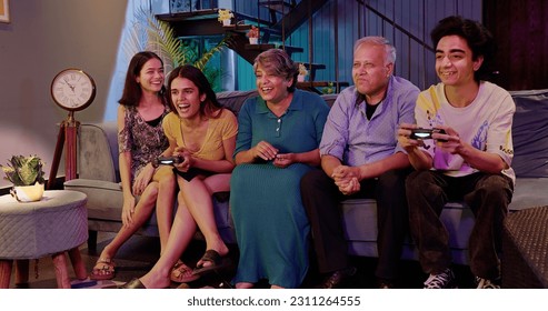 Happy Indian family sitting on sofa playing video game using controller or joystick having fun at home. Overjoyed teenage boy competing with young girl late night spend weekend engaged time together - Powered by Shutterstock