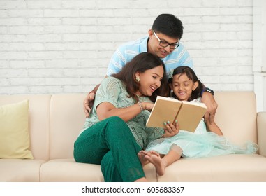 Happy Indian Family Sitting On Sofa And Reading A Book