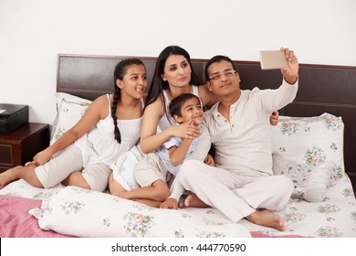 Happy Indian Family Taking Selfie Together In Bed