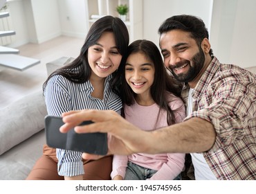 Happy indian family with teen child daughter having virtual call meeting on modern smartphone at home. Smiling dad holding cellphone looking at mobile phone taking selfie, watching video with kid.