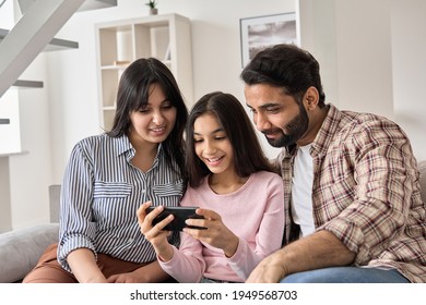 Happy indian family and teen child daughter using smart phone at home. Smiling teenage kid girl showing parents social media, watching streaming video on cellphone looking at mobile sitting on sofa.