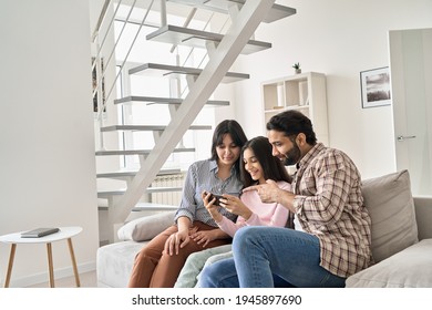 Happy indian family with teen daughter using phone together at home. Smiling parents and teenage kid girl watching social media videos, doing online shopping on smartphone in living room together.