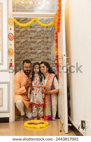 Happy indian family of three doing grah pravesh ritual or entering new house for the first time. Family sitting in front of a plate filled liquid kumkum and flowers. Griha Pravesh Concept