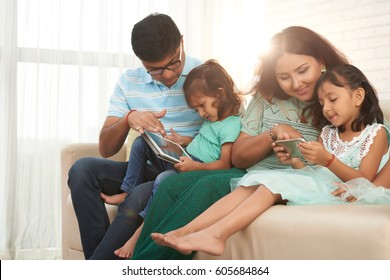 Happy Indian Family Using Smartphone And Digital Tablet At Home