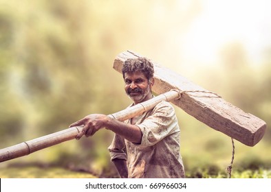 Happy Indian farmer standing with wooden plough in rice field