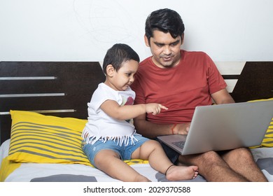 Happy Indian Father Sitting With Cute Little Adorable Daughter Using Laptop. Toddler Girl Child Pointing At Computer Screen And Dad Showing Something On Display