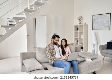 Happy indian father with teenage child daughter having fun using laptop computer at home. Smiling dad and teen kid girl watching tv movie, browsing internet, e learning sitting on sofa in modern house