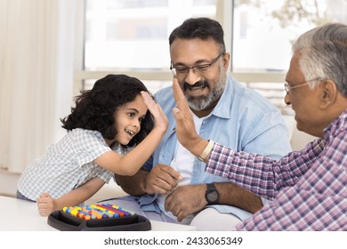 Happy Indian grandkid girl and cheerful great grandpa giving high five over colorful board game, smiling, laughing. Two grandfathers playing with granddaughter at home - Powered by Shutterstock