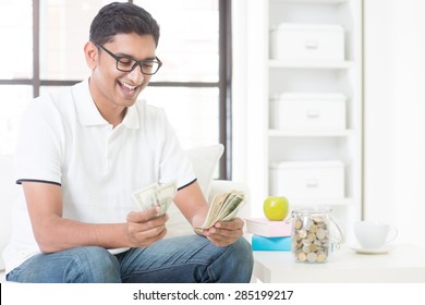 Happy Indian Guy Counting Money And Smile At Home. Asian Man Holding Cash Happily Indoor.