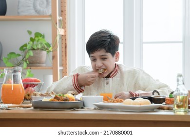 Happy Indian Handsome Boy Enjoy Eating Food With Hands, South Asian Boy Eating Naan Bread Dipping Curry, Wearing Traditional Clothes, Sitting At Dining Table At Home. Indian Culture Lifestyle