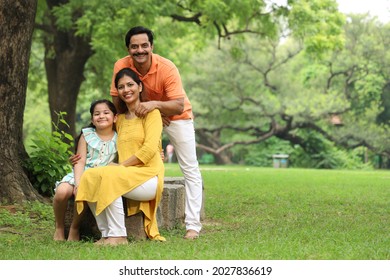 Happy Indian healthy family sitting in a city park bench having a cheerful time together. They are surrounded with greenery and serene atmosphere in peaceful and calm environment. - Shutterstock ID 2027836619