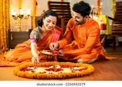 Happy indian husband helping to wife decorating rangoli with flowers for diwali festival celebration while sitting on floor at home - concept of relationship, bonding, and religious ceremony - Powered by Shutterstock