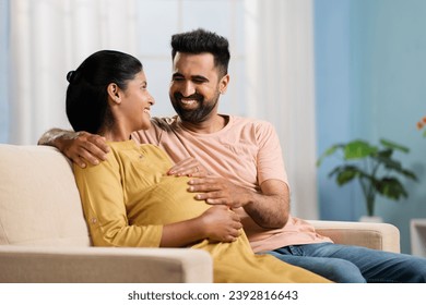 Happy Indian husband showing laptop to pregnant wife at home - concept of parenthood, cyberspace and surfing internet. - Powered by Shutterstock