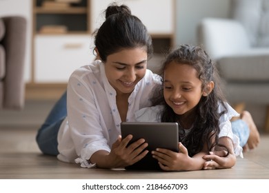 Happy Indian little kid and mom using digital tablet, resting on heating floor at home, smiling, laughing. Mother and child enjoying leisure, watching movie, reading book online - Powered by Shutterstock