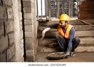 Happy Indian male construction worker constructing brick wall - hard working concept, manual labour - Powered by Shutterstock