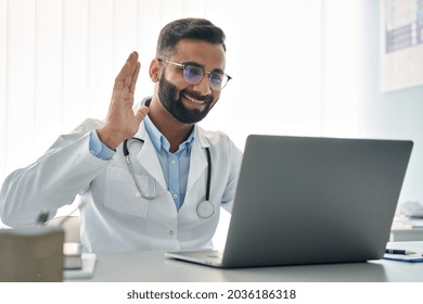 Happy Indian Male Doctor Waving Hand Having Virtual Video Call Online Consultation On Laptop Computer In Hospital. Tele Health Medicine. Telemedicine Patients Appointment Distance Remote Chat In India