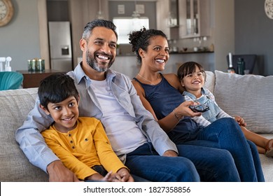 Happy indian man and african woman relaxing with daughter and son watching television at home together. Cheerful ethnic family relaxing on sofa at home watching movie with children.  - Powered by Shutterstock