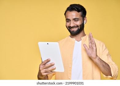 Happy Indian Man Using Digital Tablet Standing Isolated On Yellow Background. Smiling Ethnic Guy Wearing Earbud Waving Hand Having Remote Video Call, Remote Online Distance Learning Conference Class.