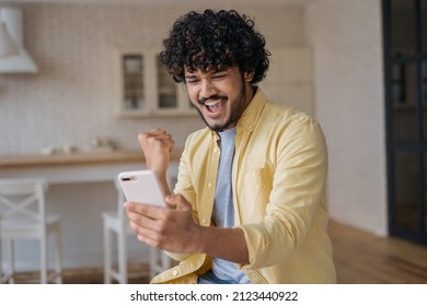 Happy Indian man using smart phone playing mobile game. Young excited asian gambler holding mobile phone win money celebration success, sport betting concept. Emotional  freelancer receive payment - Shutterstock ID 2123440922