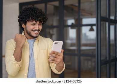 Happy Indian Man Win Online Sports Betting Celebration Victory At Home. Excited Asian Guy Using Mobile Phone Watching Football Game. Emotional Male Playing Mobile Game, Copy Space  