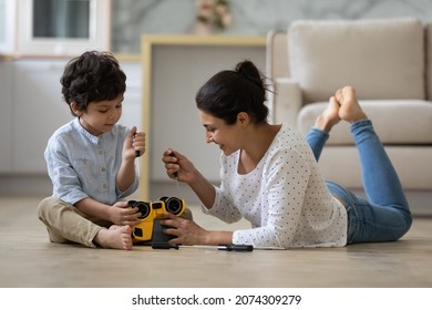 Happy Indian mom and little son playing motor mechanic games with on heating floor, repairing toy plastic car with screwdrivers. Father and kid enjoying playtime, development activities at home