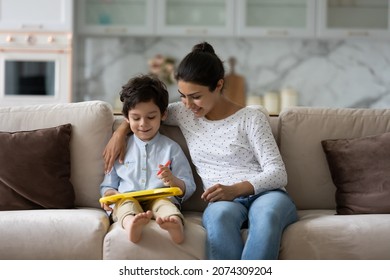 Happy Indian mom teaching little son to draw  Babysitter watching kid using toy board pencil  Young mother   child enjoying developing activities at home  playing couch  Motherhood  upbringing
