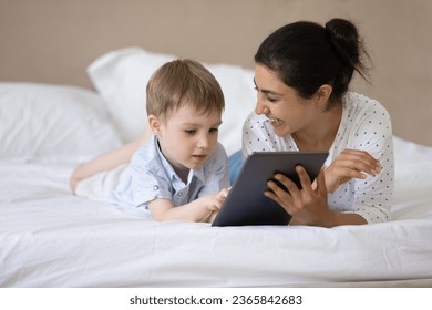 Happy Indian mother with 7s son using tablet together, relaxing lying on cozy bed at home, smiling caring young mom and adorable boy child having fun with device, watching cartoons, enjoying weekend - Powered by Shutterstock