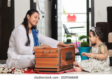 Happy Indian Mother Teaching Her Cute Little  Daughter To Play Harmonium At Home. Young Woman And Small Girl Child, Spend Time Together. Practicing Learning Musical Instrument, Music Class.