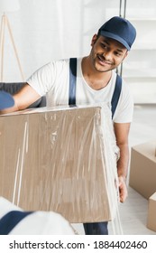 Happy Indian Mover Holding Wrapped In Stretch Film Box Near Worker On Blurred Foreground 