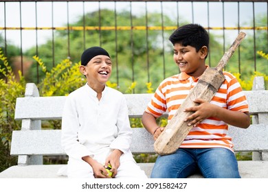 Happy indian multiethnic children talking about cricket with bat and ball sitting at park - concept of childhood friendship, holidays, vacation activities and communal harmony