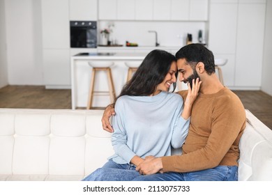 Happy Indian Newlyweds Moved In New Apartment, Sitting At The Sofa In Embraces, Looking At Each Other. Multi Ethnic Couple In Love Rent A House Together. Relocated In New Home Concept