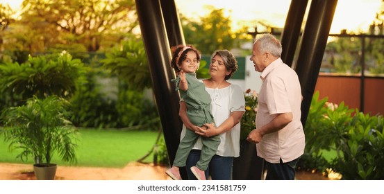 Happy Indian old grandmother standing holding cute little child girl in arms hands playing together outdoor home. Beautiful senior couple talking with small adorable daughter enjoying summer holiday - Powered by Shutterstock